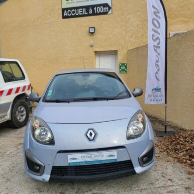 Renault Twingo d'occasion bleu clair devant Detail Auto à Pamiers avec panneau Accueil à 100m.