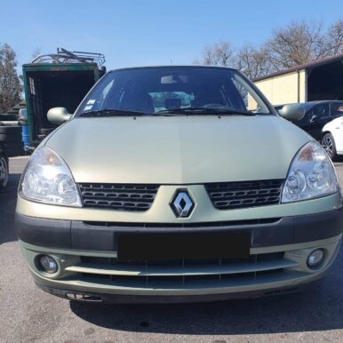 Face avant d'une Renault Clio II verte d'occasion stationnée sur un parking sous un ciel bleu ensoleillé.