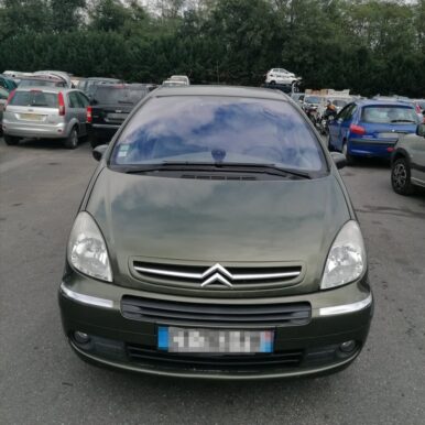 Citroën Xsara Picasso vert olive stationnée dans une casse automobile entourée d'autres véhicules d'occasion.